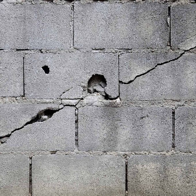 Cracked gray cinderblock wall with a small hole and diagonal damage line