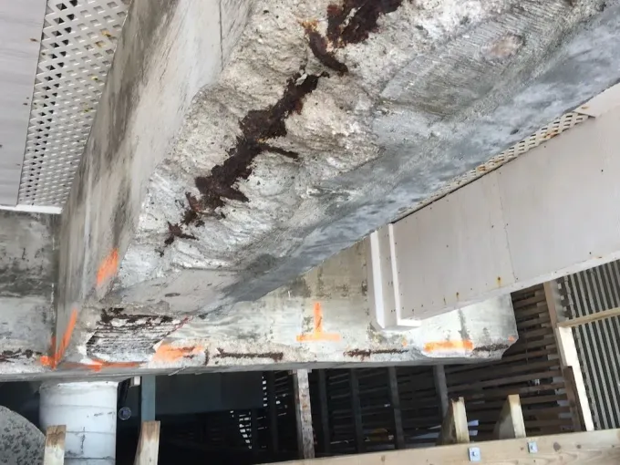 Corroded concrete beam with exposed rust in an industrial structure