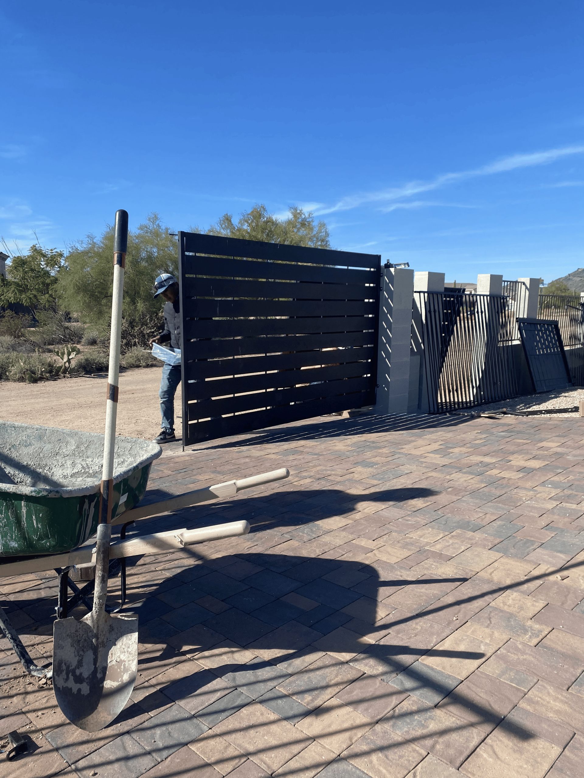 Black wooden gate and slatted fence on a gravel path under a bright blue sky.