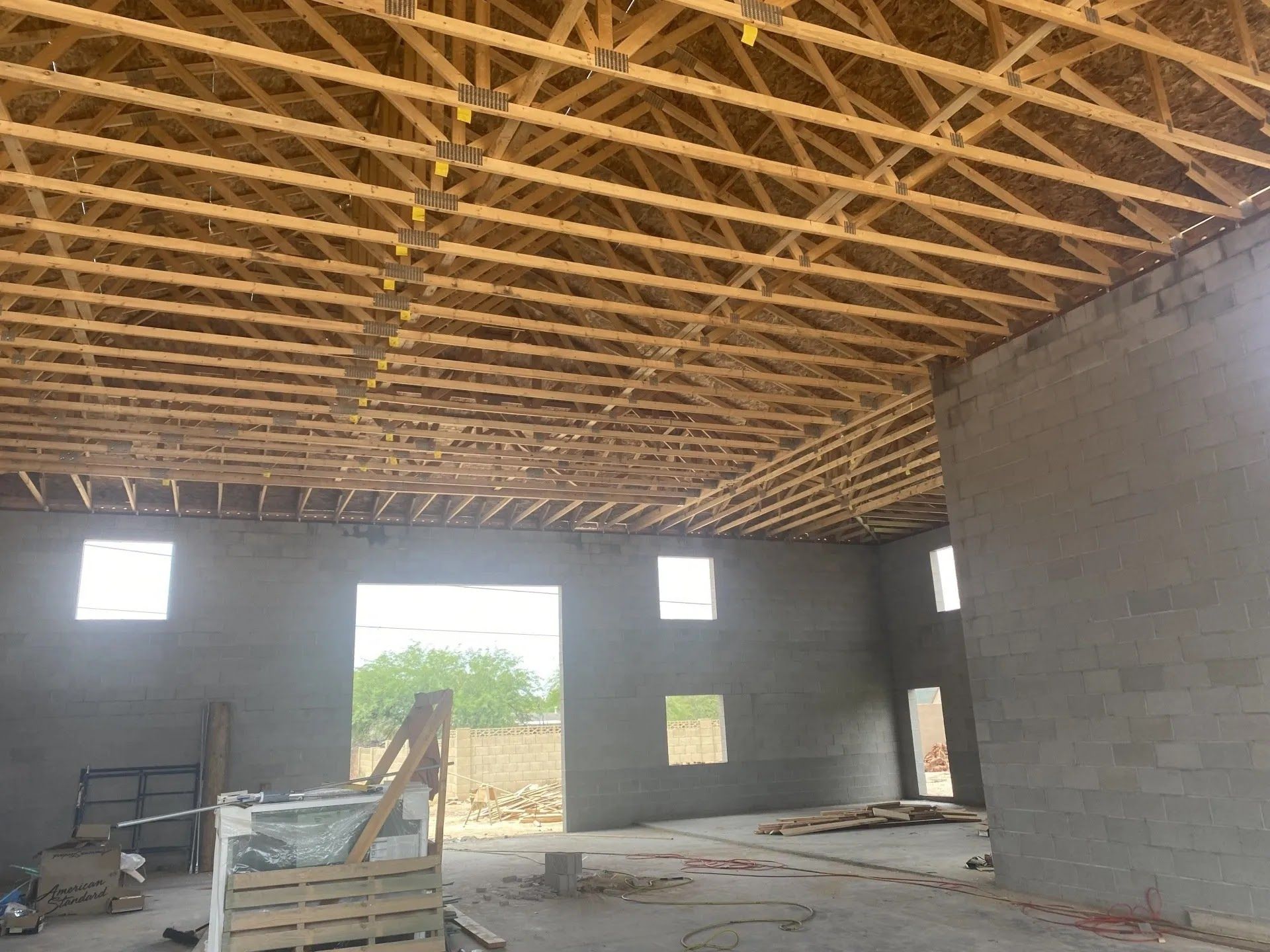 Interior of unfinished building with exposed wooden roof trusses, gray block walls, and open doorways and windows.