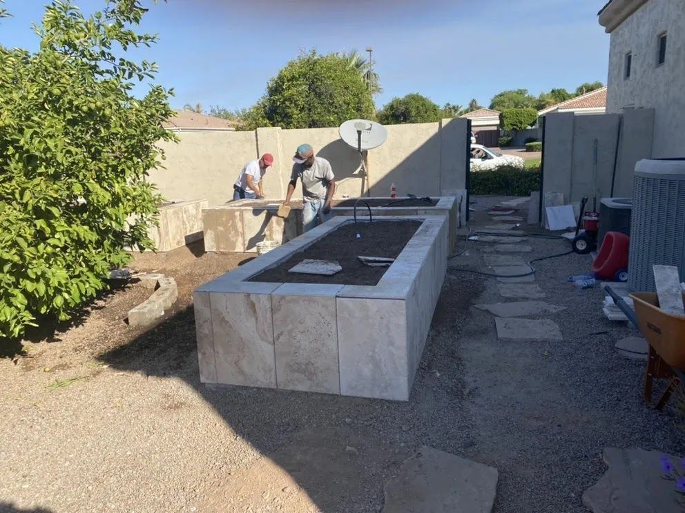 Backyard construction site with workers building a raised stone structure beside a house