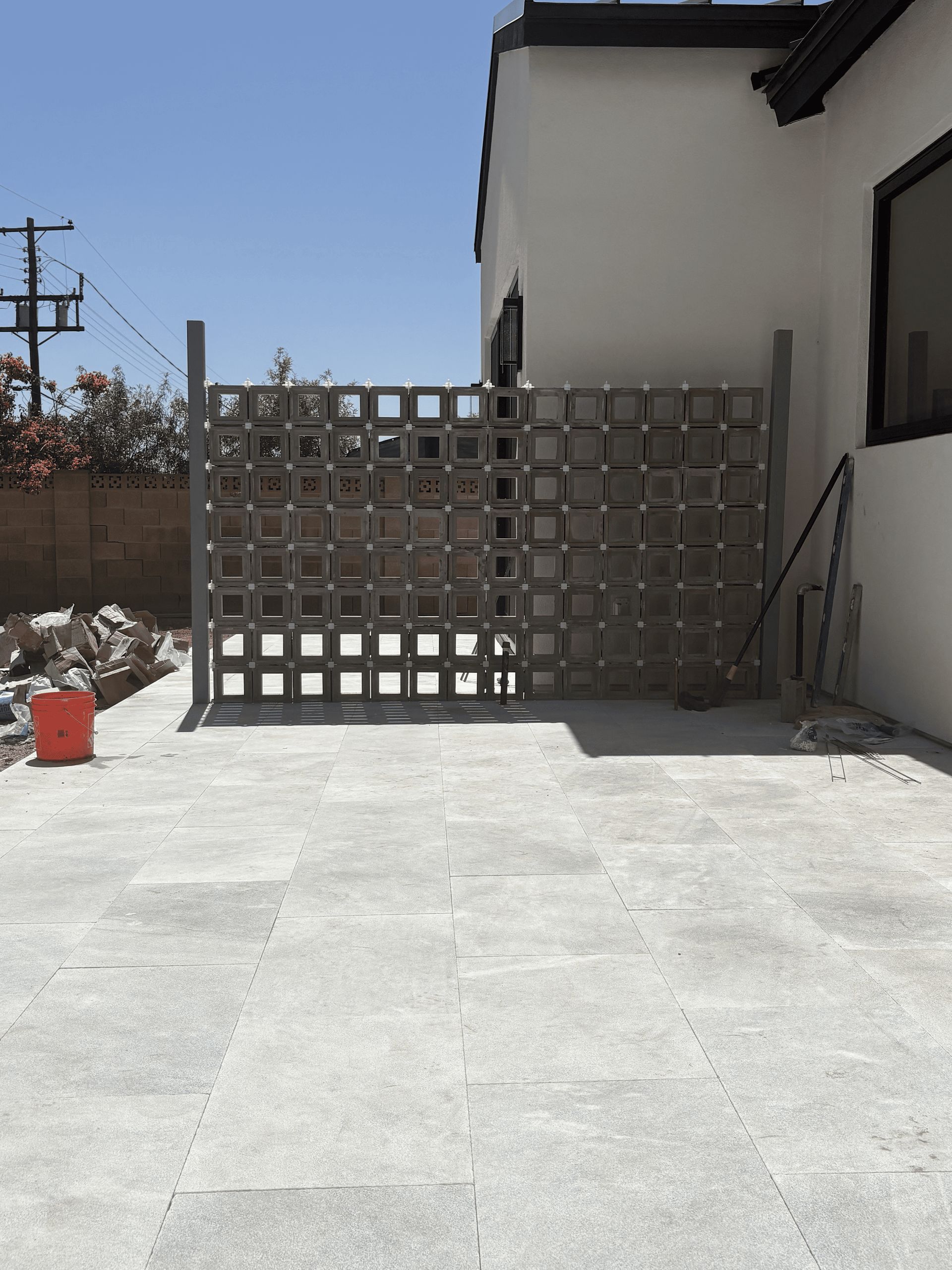 Concrete patio beside a white house, with a gray lattice fence and construction materials in the background