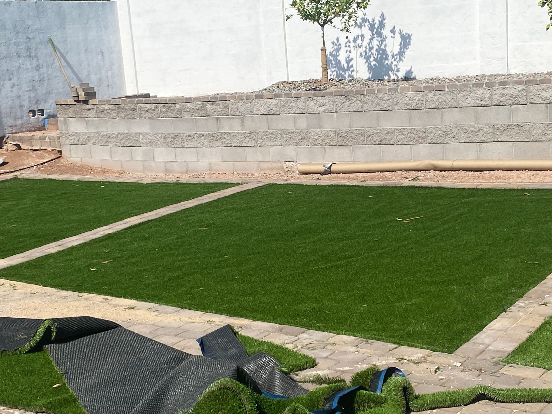 Concrete retaining wall beside a green lawn with stone paths and scattered construction materials