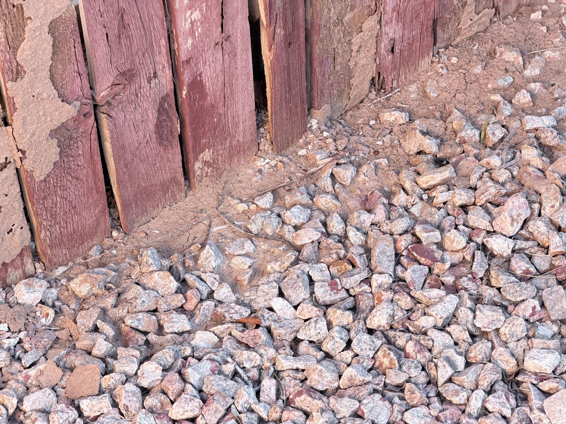 Close-up of weathered red wooden fence above a pile of gray and pink gravel.