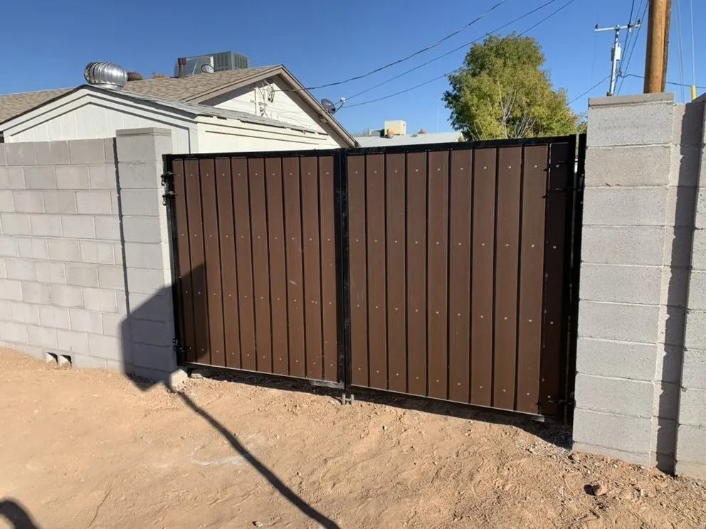 Brown metal driveway gate between gray cinderblock walls at a house entrance