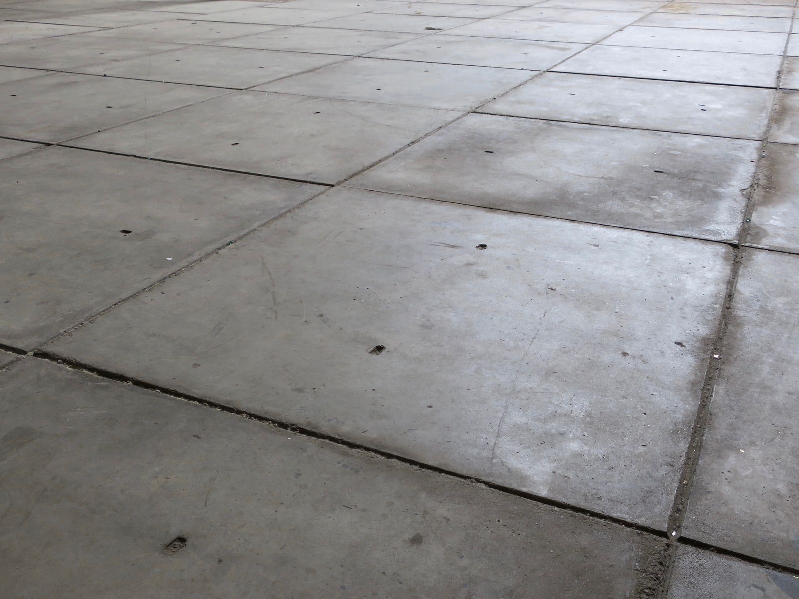 Wet concrete pouring from a truck chute onto a construction site, forming a gravelly slab surface