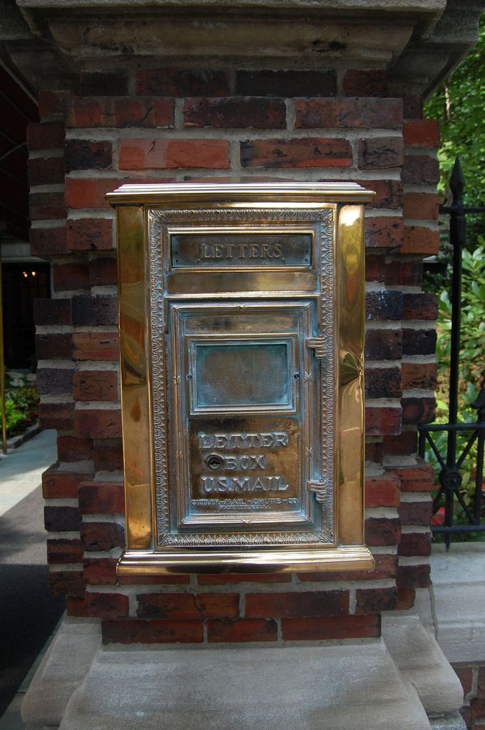 Brass mailbox mounted on a red brick pillar beside a walkway