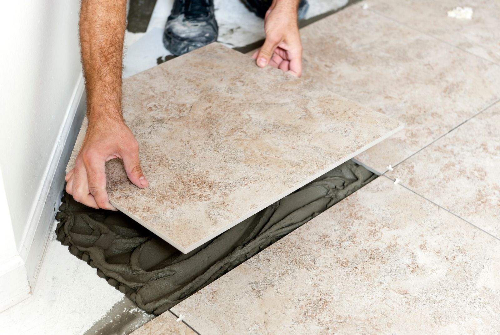 Hands lifting a tile to reveal fresh mortar underneath on a tiled floor