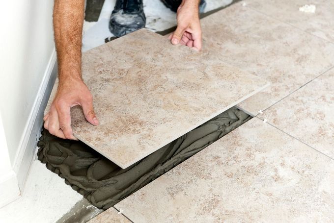 Person lifting a tile to apply mortar beneath a floor repair