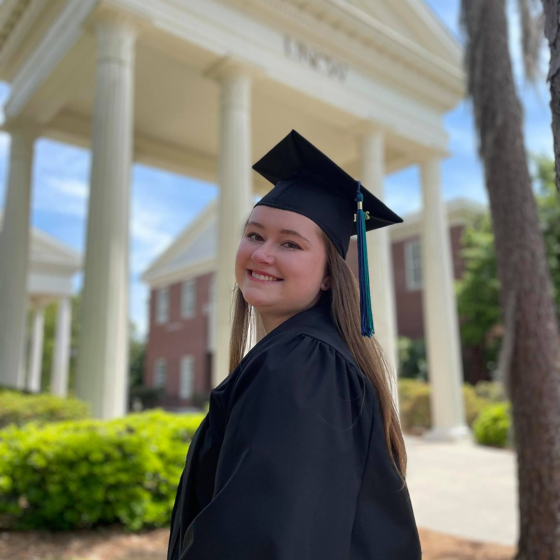 Marisa Moore in graduation gown and cap near Morton Hall, UNCW campus