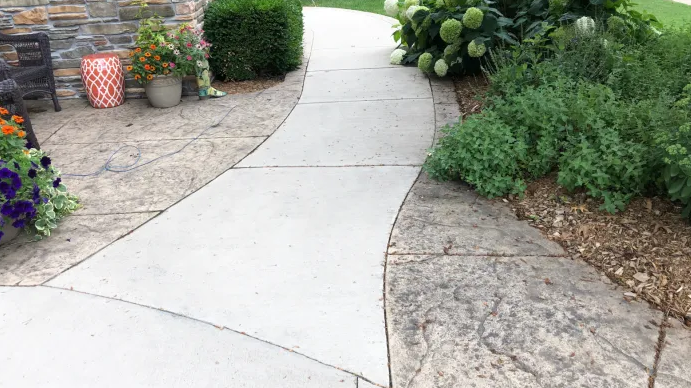 A concrete walkway leading to a patio with flowers on the side.