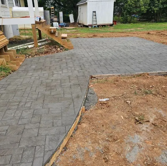 A man is working on a concrete patio in front of a brick house.
