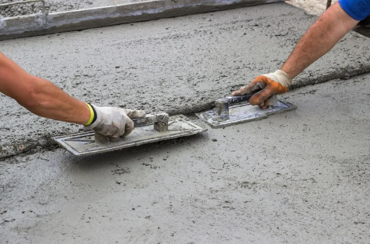 A man is working on a concrete patio in front of a brick house.