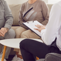 Therapist taking notes while speaking with two seated clients in a 상담 room