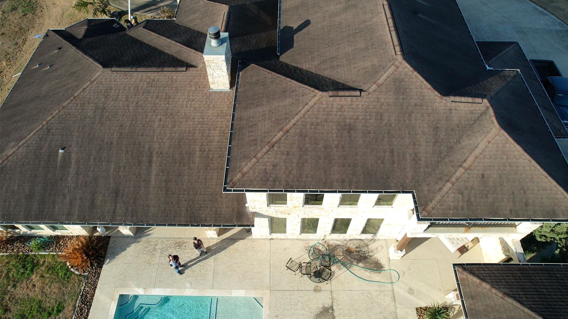 Overhead view of a large house with brown roof and a blue pool in the front.