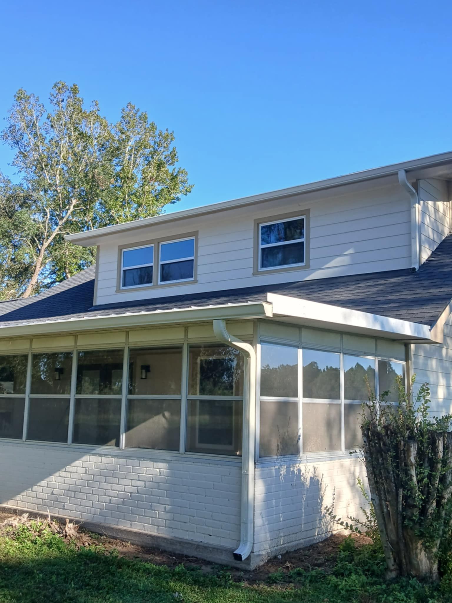 Two-story house with a screened porch, windows, and light siding against a blue sky.