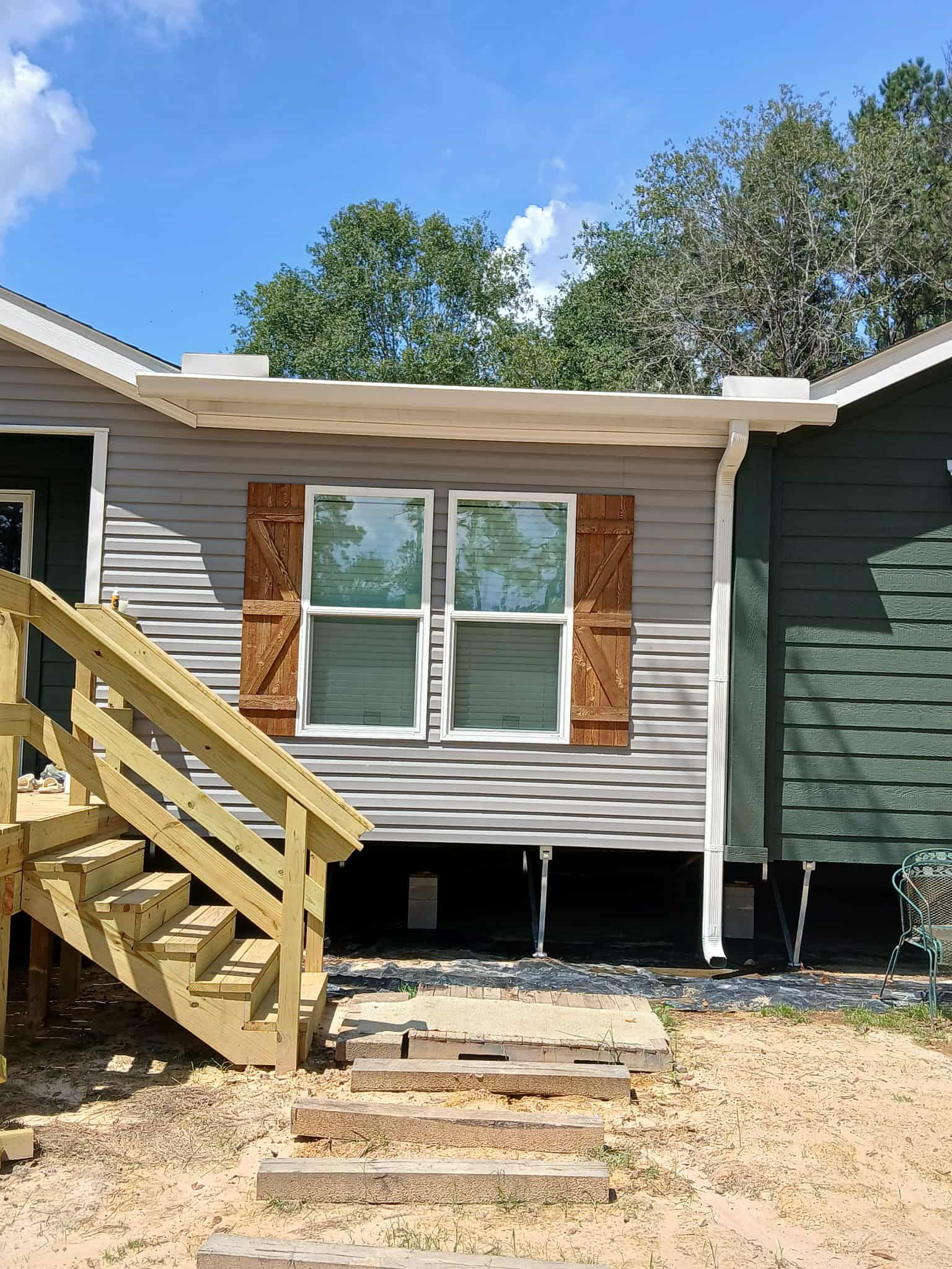Exterior view of a house with gray siding, brown shutters, and wooden stairs leading up to a doorway.
