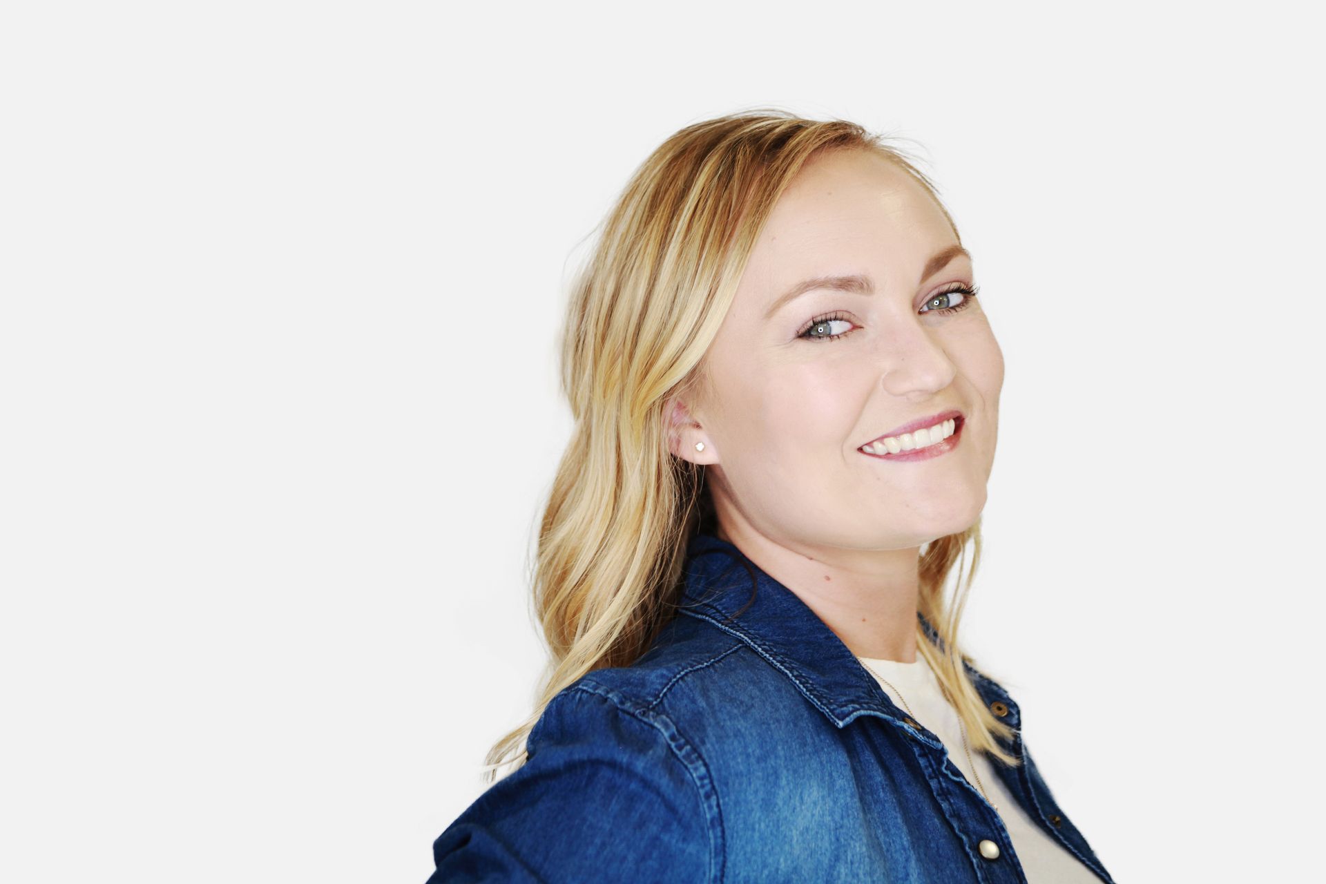 A woman in a denim jacket is smiling and looking at the camera.
