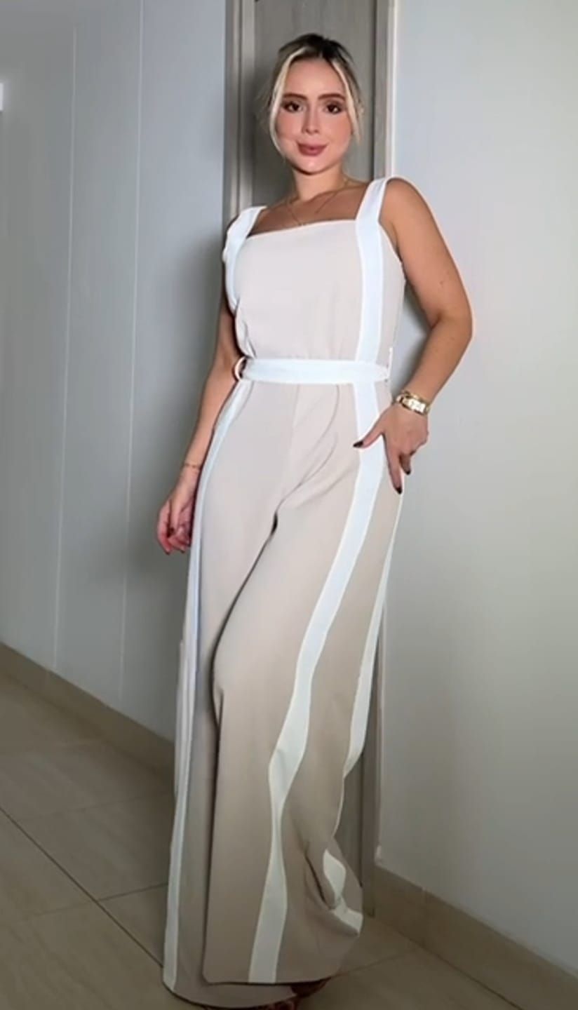 Mujer con un mono color canela con ribete blanco, de pie cerca de una pared.