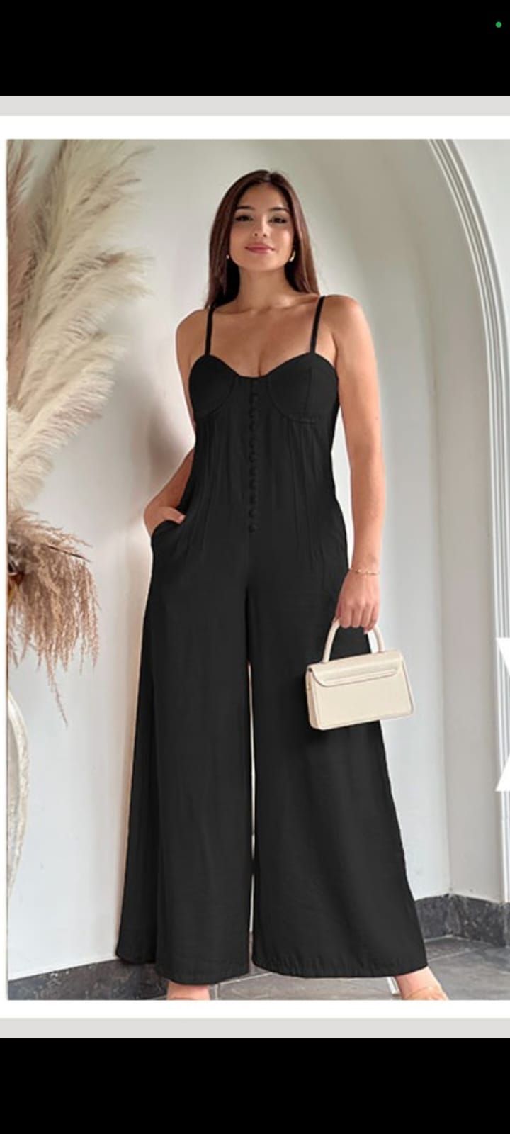 Mujer con mono negro y un pequeño bolso blanco, posando en el interior.