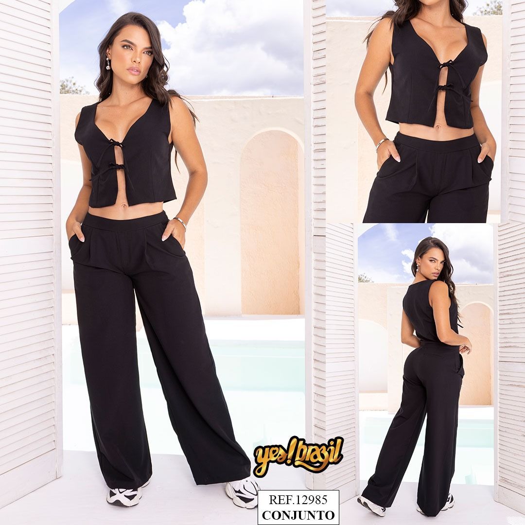 Una mujer con un traje negro posa frente a un fondo neutro. El atuendo incluye una blusa sin mangas y pantalones anchos.