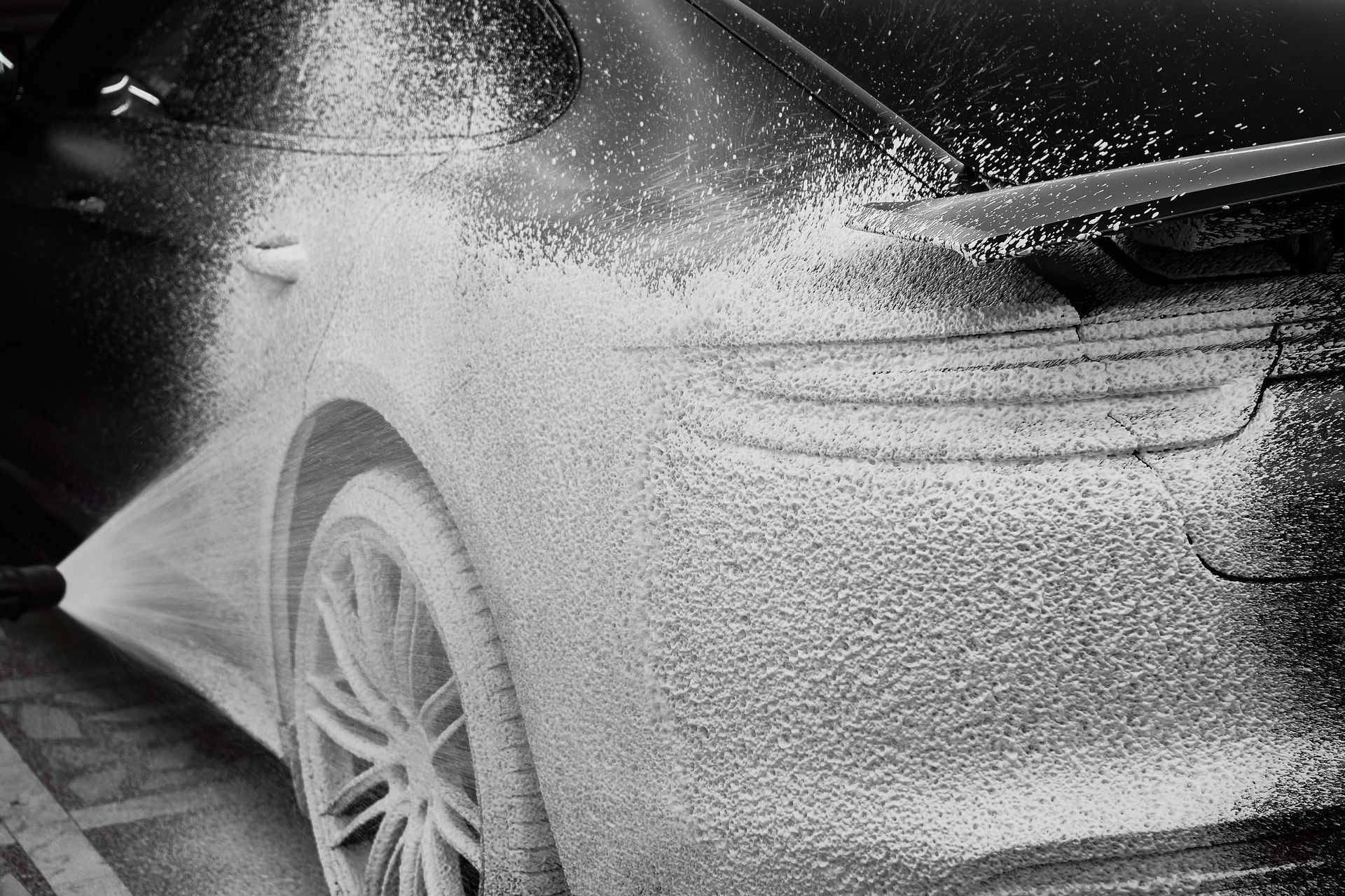 Black car being sprayed with foamy soap at a car wash.
