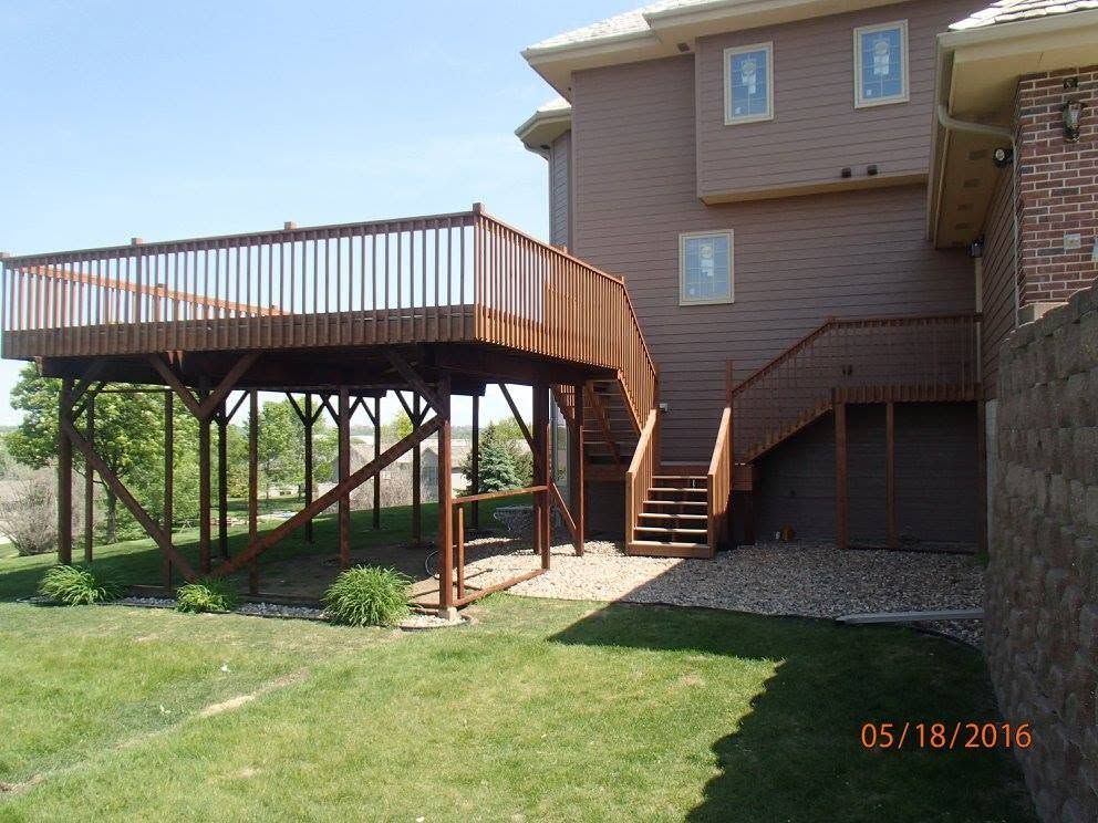 Backyard deck with stairs beside a tan house, overlooking a grassy lawn.