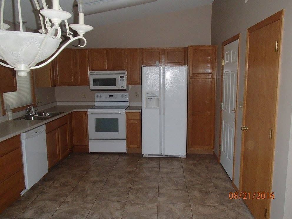 Empty kitchen with wood cabinets, white appliances, and tiled floor