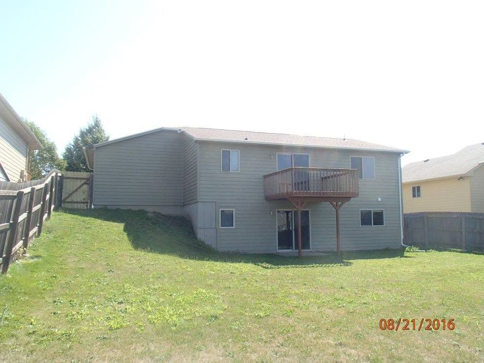 Suburban house with tan siding, small balcony, and grassy backyard on a sunny day