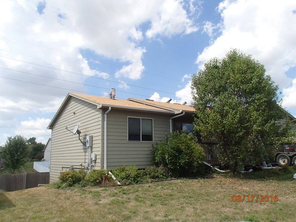 Single-story beige house with a tree and cloudy blue sky, viewed from the yard