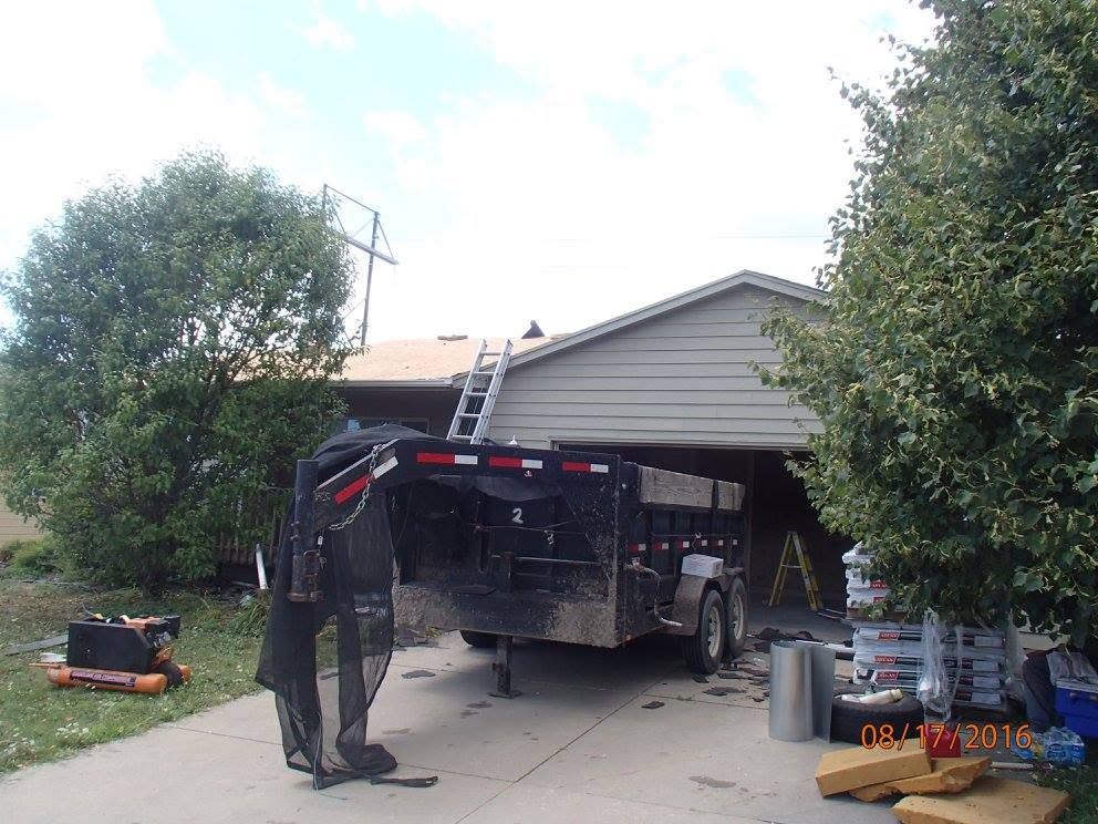 Worker near black utility truck with ladder parked in driveway by a garage