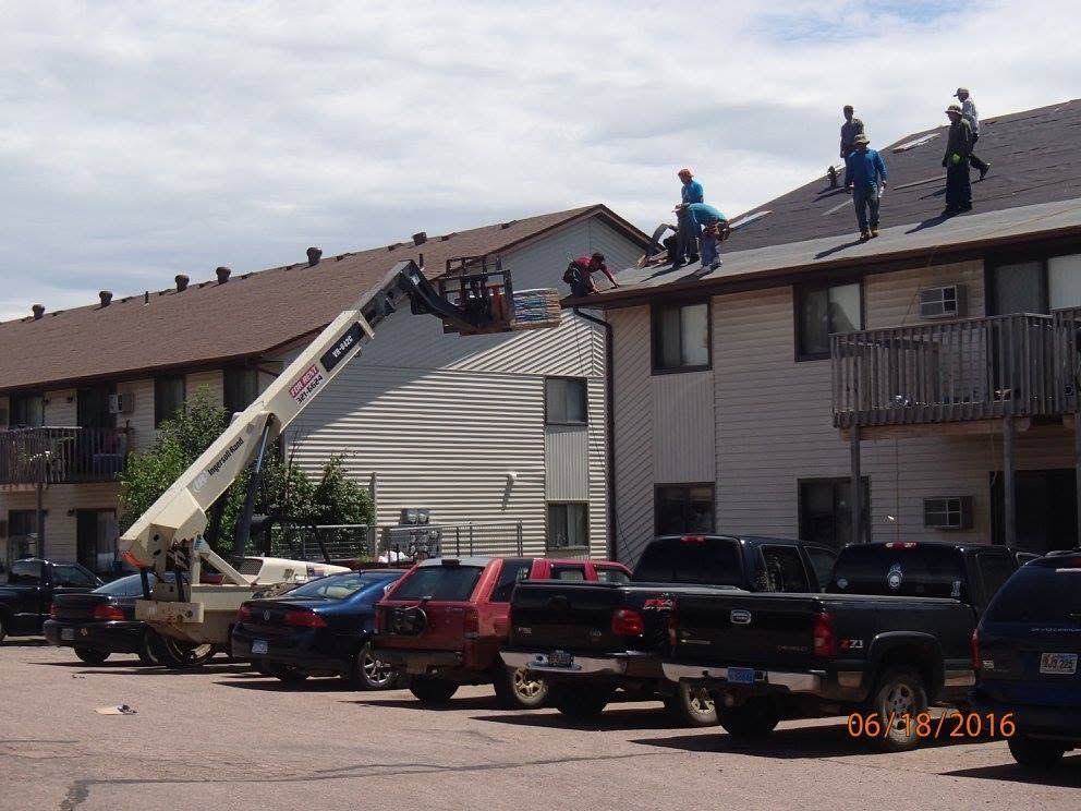 Firefighters on a ladder truck working on a roof above parked cars and an apartment building