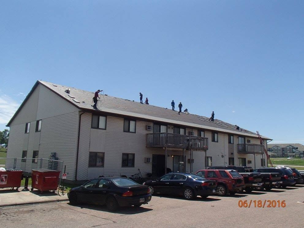Apartment building with workers on the roof and parked cars in front