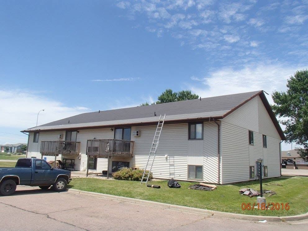 Single-story beige apartment building with a ladder leaning against the side and a pickup truck parked nearby