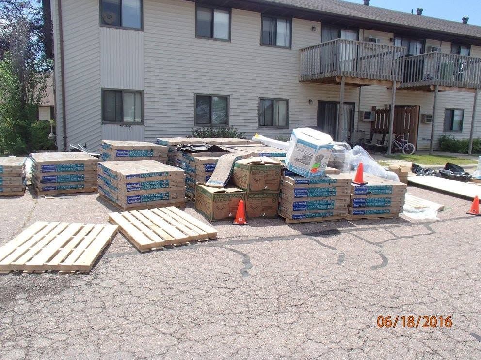 Stacks of building materials and wood pallets outside an apartment building courtyard.