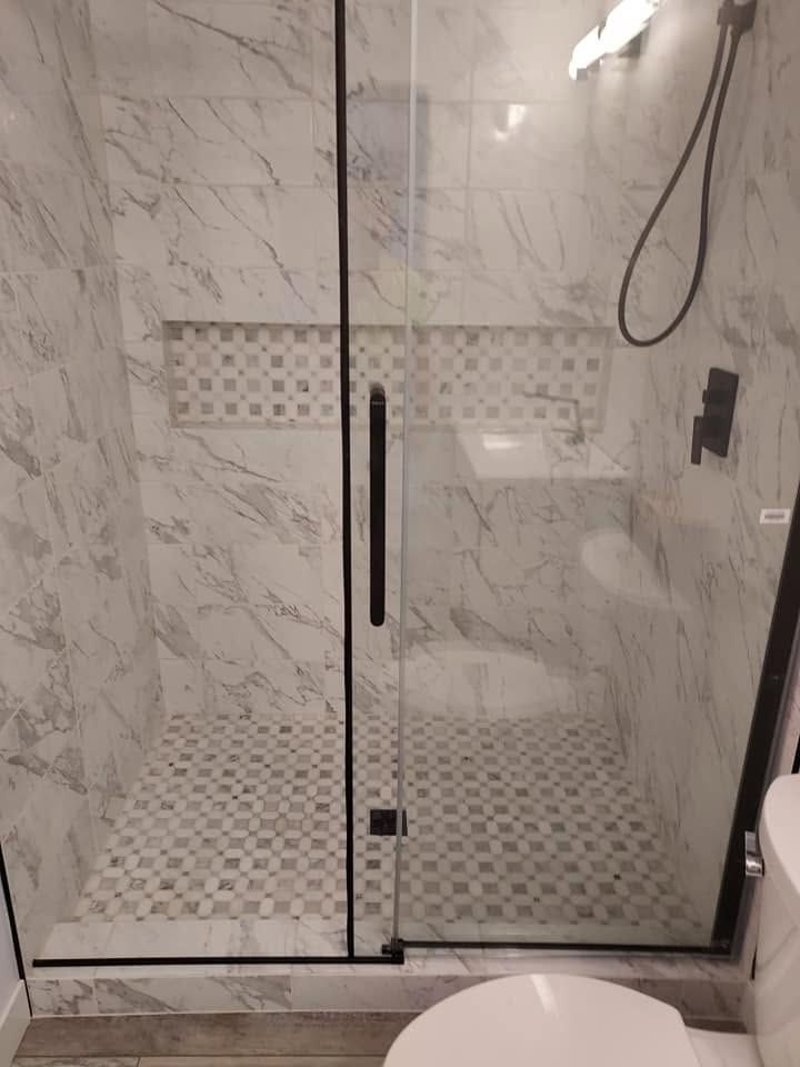 Glass shower enclosure with marble tile walls and patterned floor in a bathroom