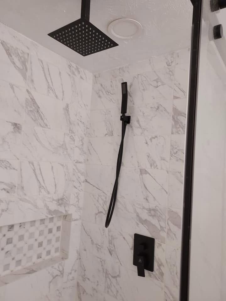 Modern shower with white marble tile, black fixtures, and a handheld shower wand.