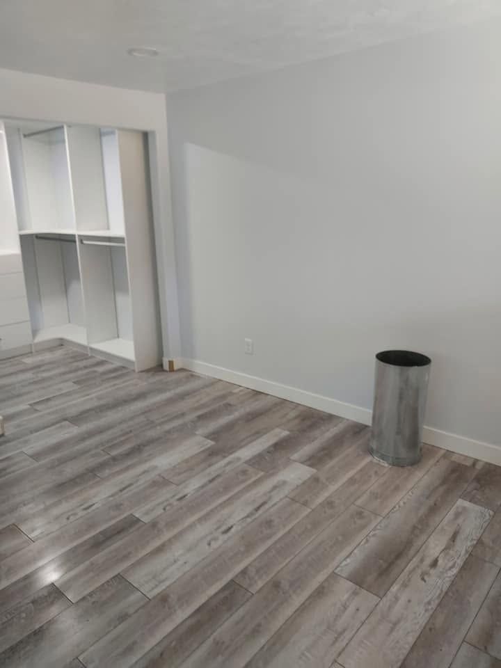 Empty room with gray wood-look flooring, white walls, built-in shelving, and a metal trash can.
