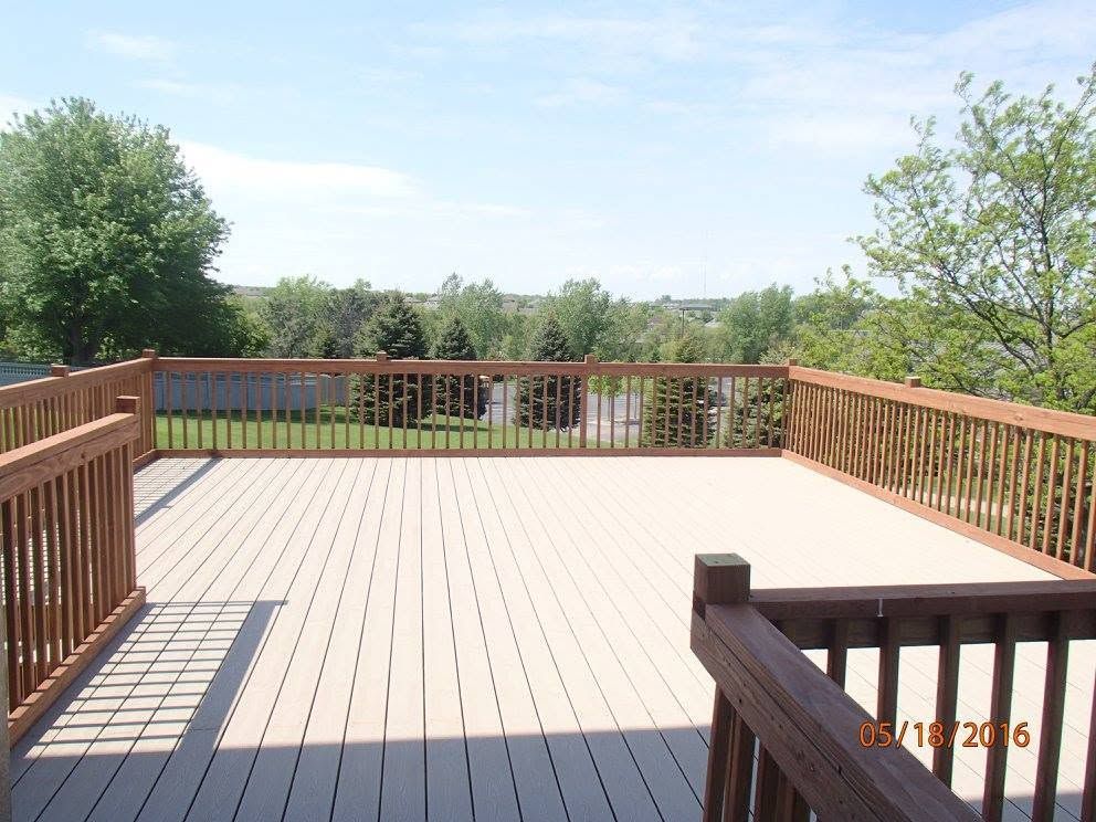 Wooden deck with railings overlooking a green wooded landscape under a clear sky.