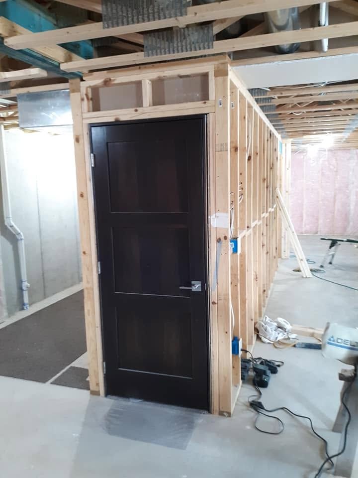 Black door in a framed wall under construction with exposed beams and tools on the floor.