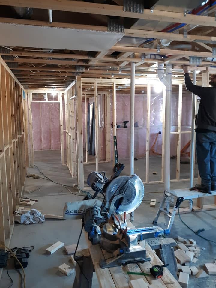 Interior of a house under construction with exposed framing, drywall tools, and a miter saw on the floor