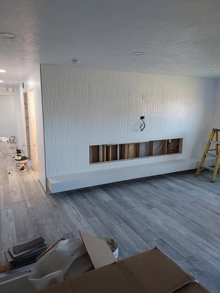 Partially renovated living room with gray flooring, white wall cutout, and ladder on the right