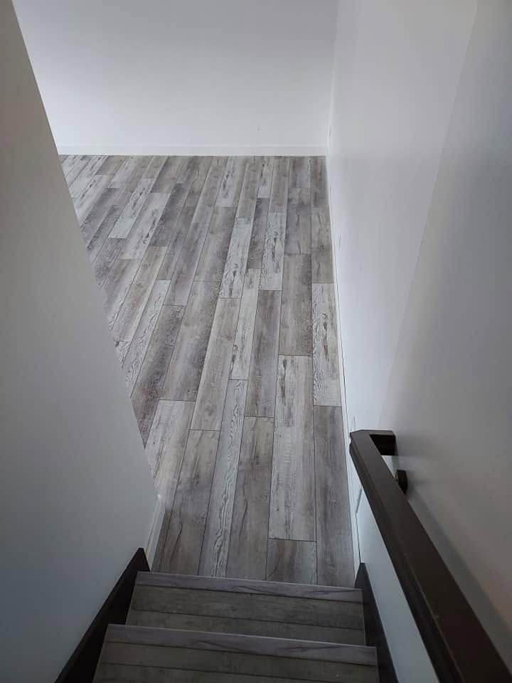 Staircase leading down to a room with gray wood flooring and white walls