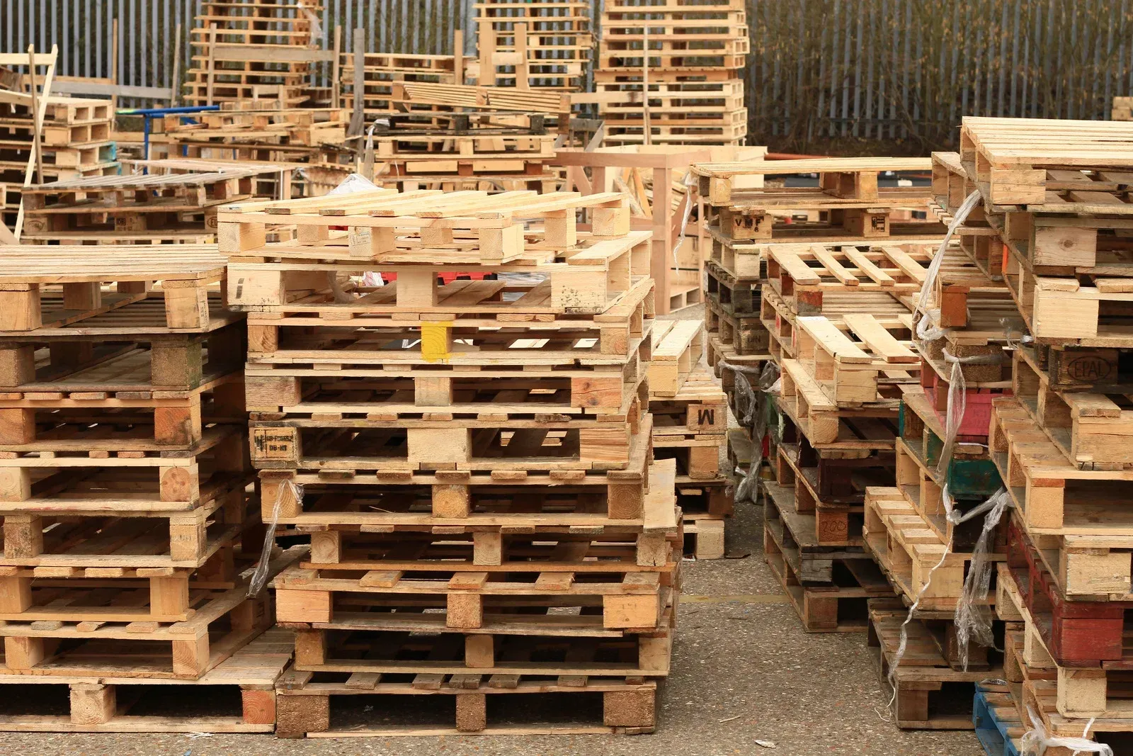 Stacks of wooden shipping pallets in an outdoor lot, showing varying colors and wear.