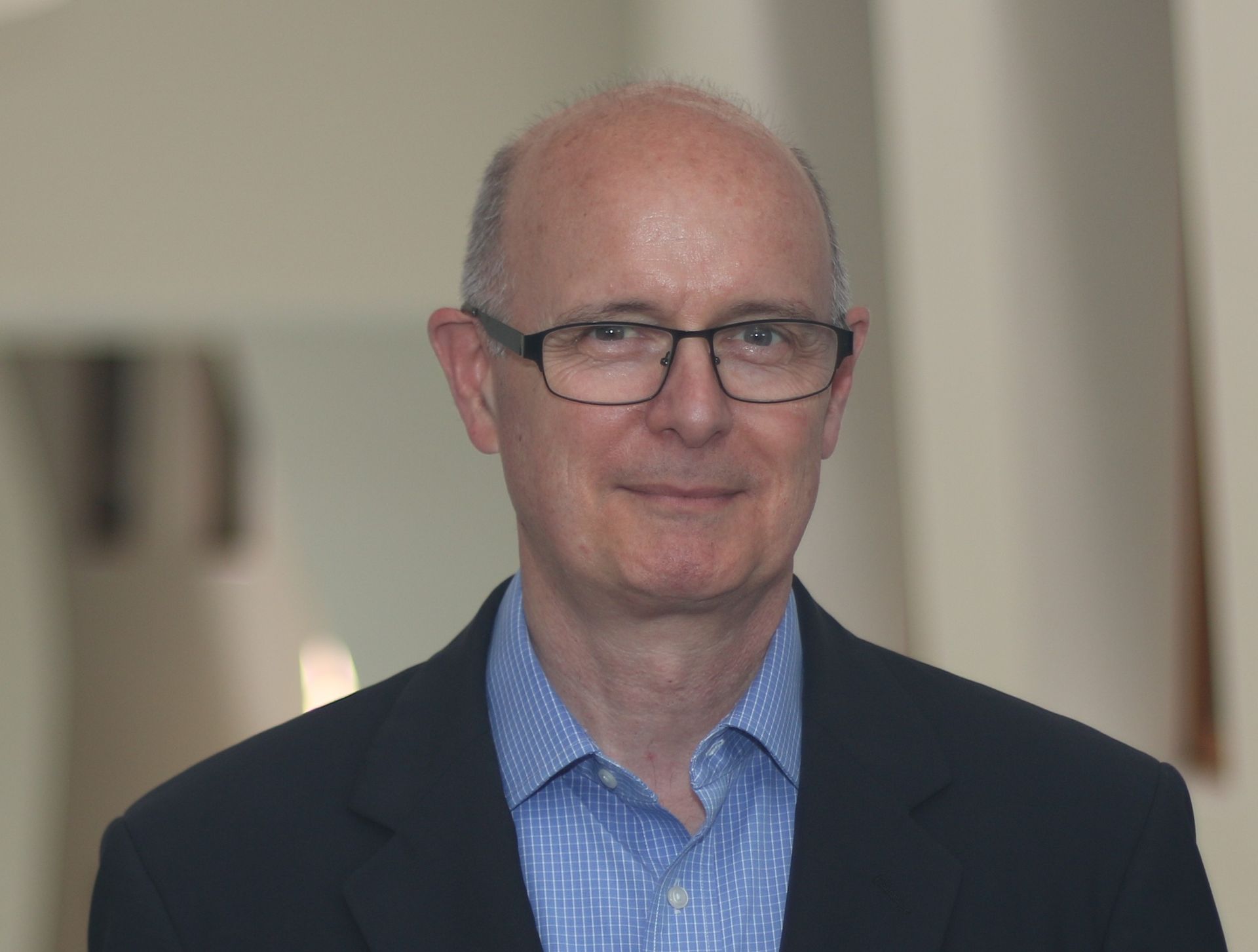 Portrait of a man in glasses and a dark blazer against a softly blurred indoor background