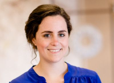 Woman with dark hair, wearing a blue shirt, smiling, looking at the camera.
