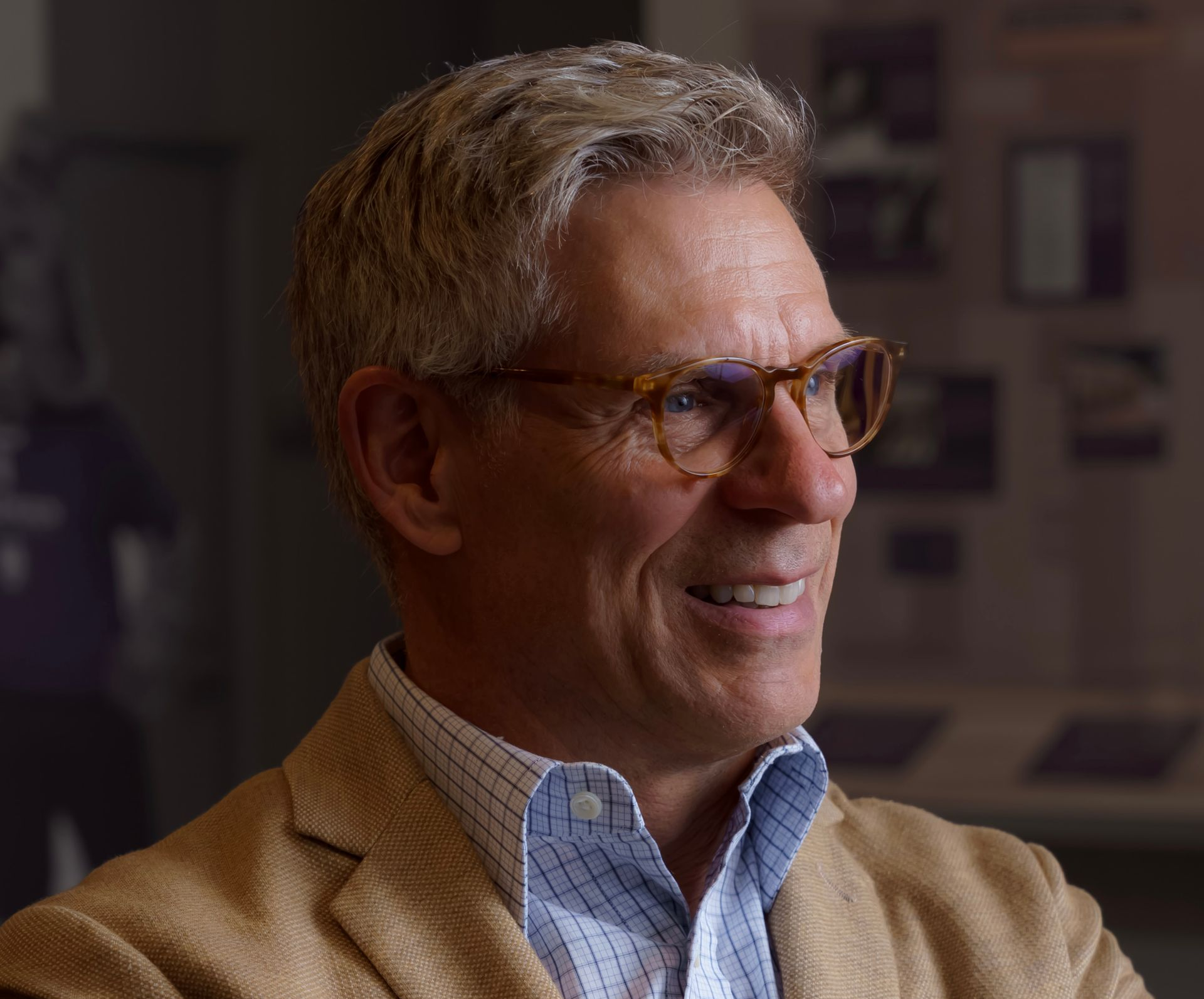 Man wearing glasses, light jacket, and button-down shirt, smiling in a room with displays.