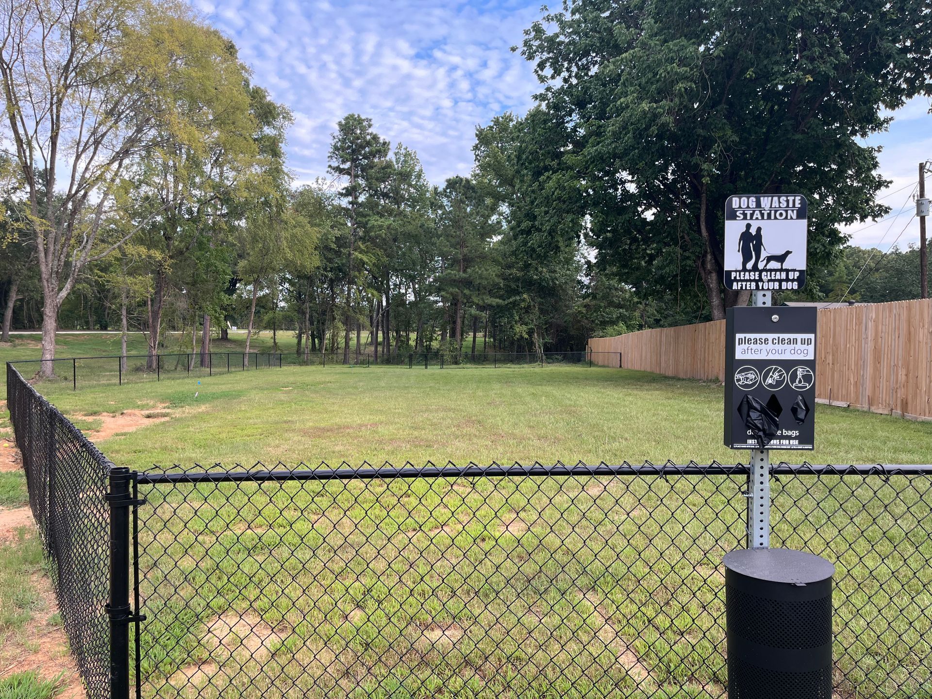 A dog park with a chain link fence and trees in the background.