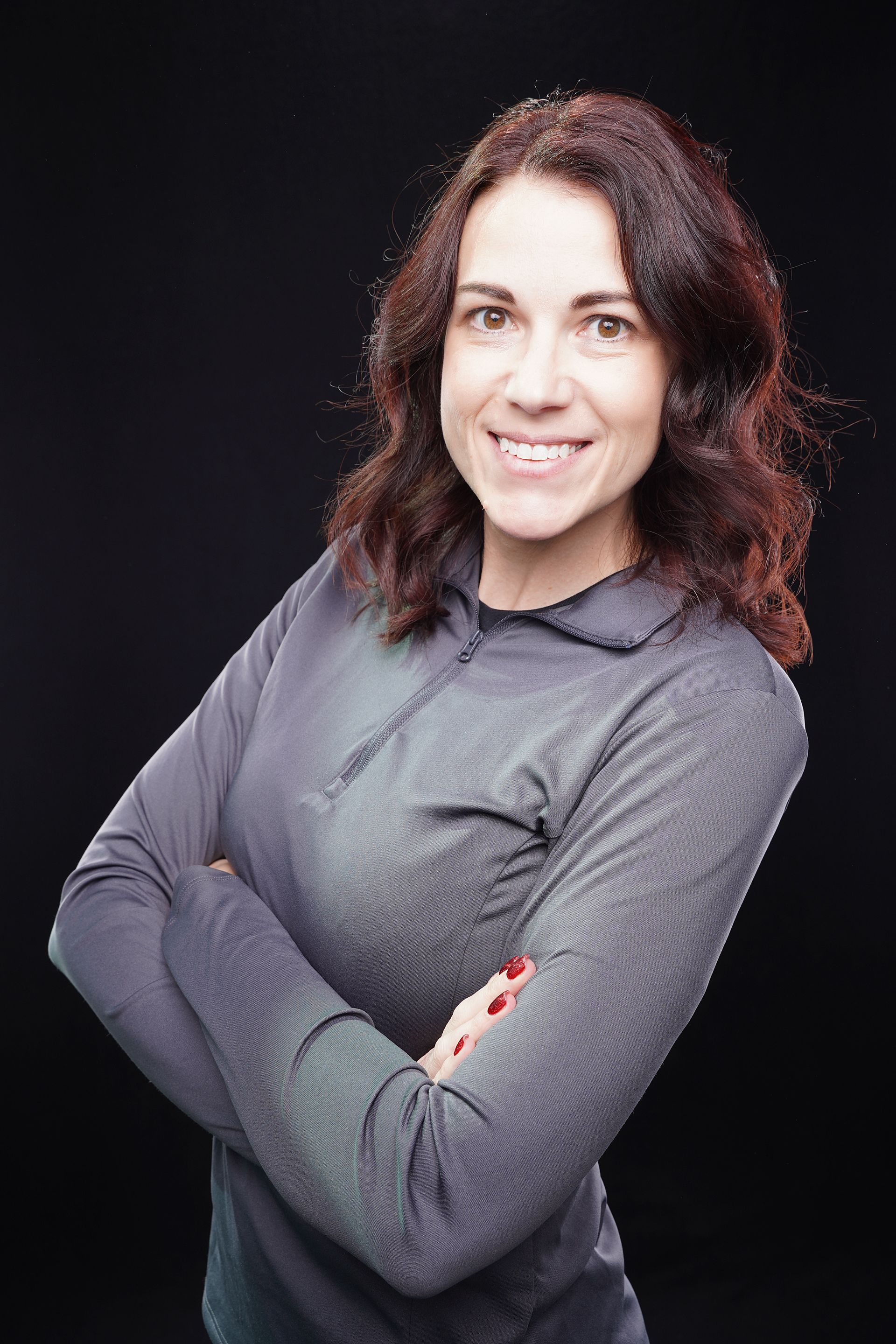 A woman in a red shirt is posing for a picture with her arms crossed.