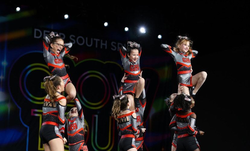 A cheerleader is being lifted in the air by two other cheerleaders.